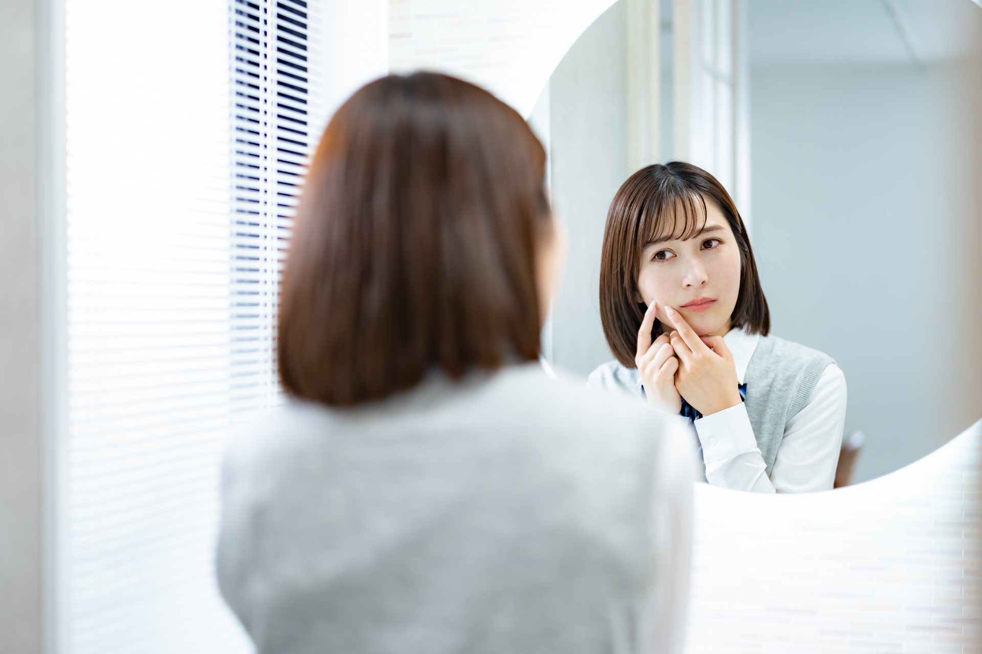 鏡を見てニキビに悩む若い女性